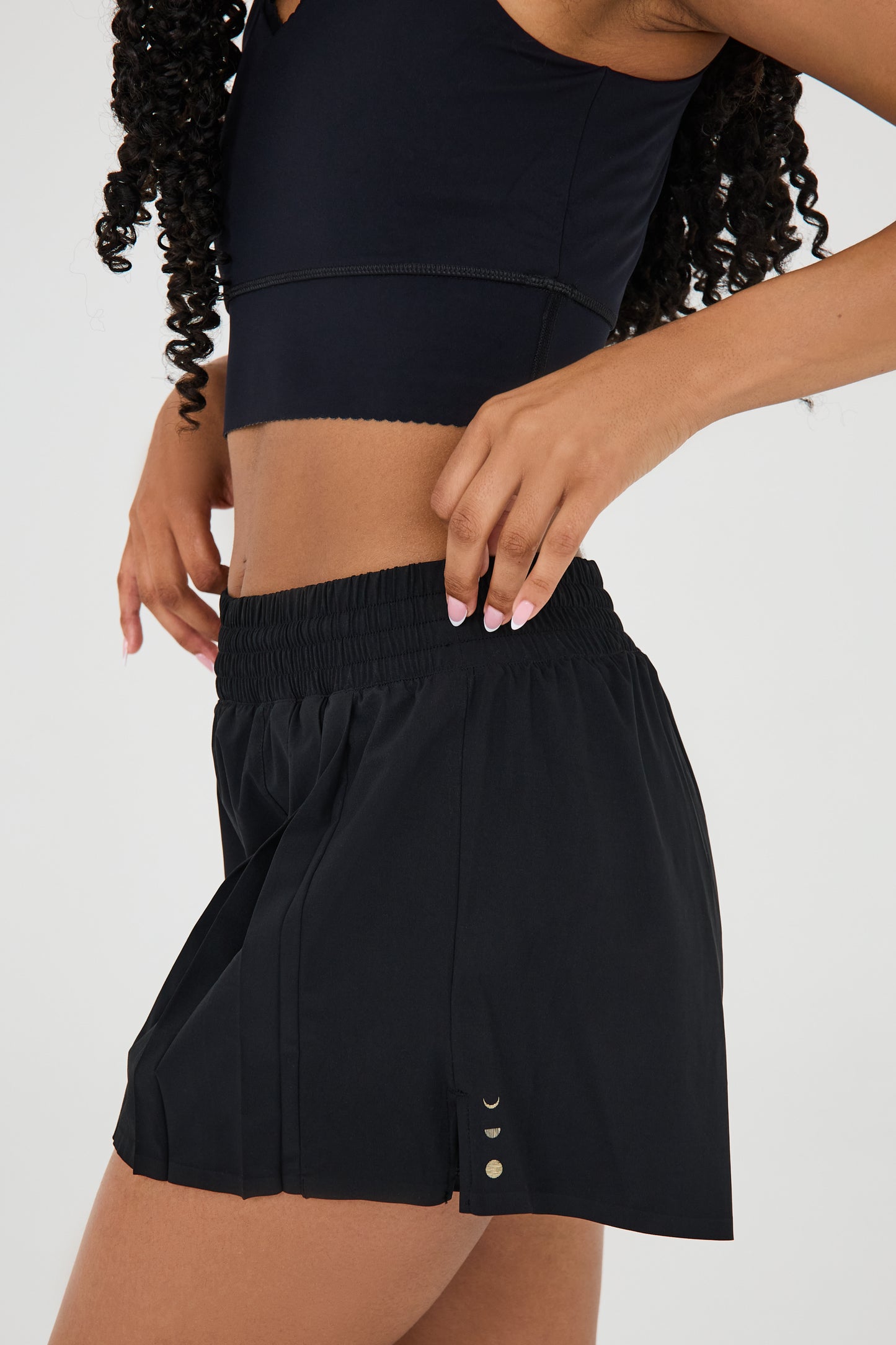 Model wearing L’Original Flowy Short featuring a featherlight pleated outer layer and a sculpting compressive inner short. The 2-in-1 design blends feminine movement with performance support, including patented MicroPerle® bead infusion and a hidden inner pocket for essentials like a phone or tennis ball.