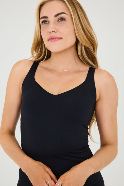 Model wearing the black Iconic Tank in a sculpting, compressive fit with an elevated neckline and built-in bra. Designed with MicroPerle® beads along the back panel for lymphatic stimulation and posture support, this sleek tank transitions effortlessly from activewear to refined layering piece.