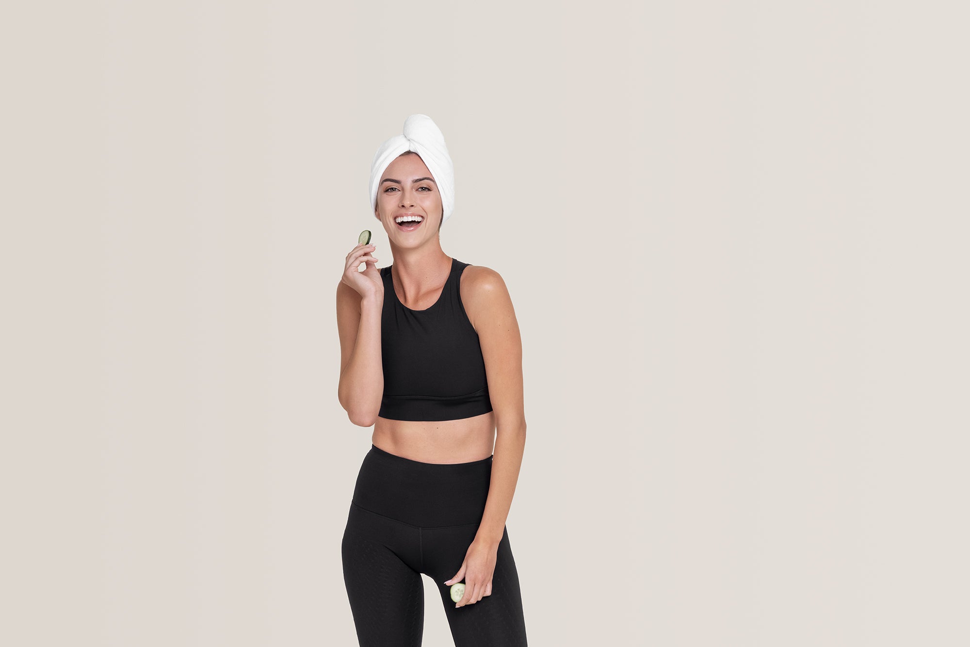 Model posing in Black set with towel wrapped around head holding cucumber slice