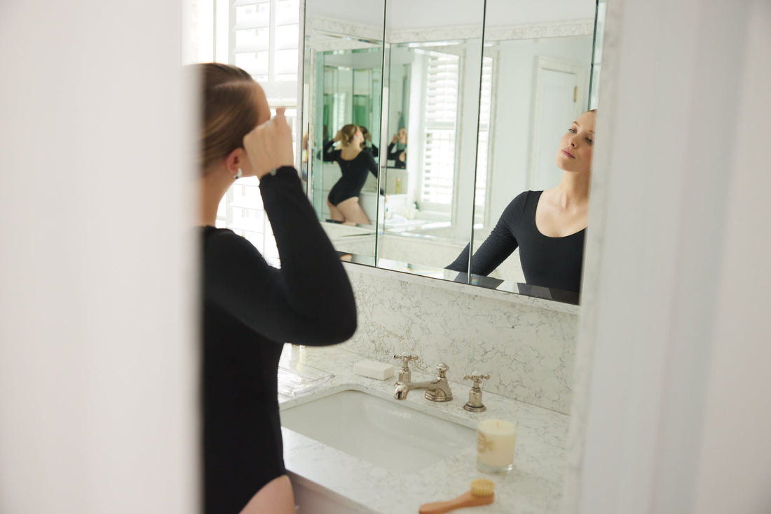 Model wearing Elastique long sleeve bodysuit looking at her reflection in a mirror.