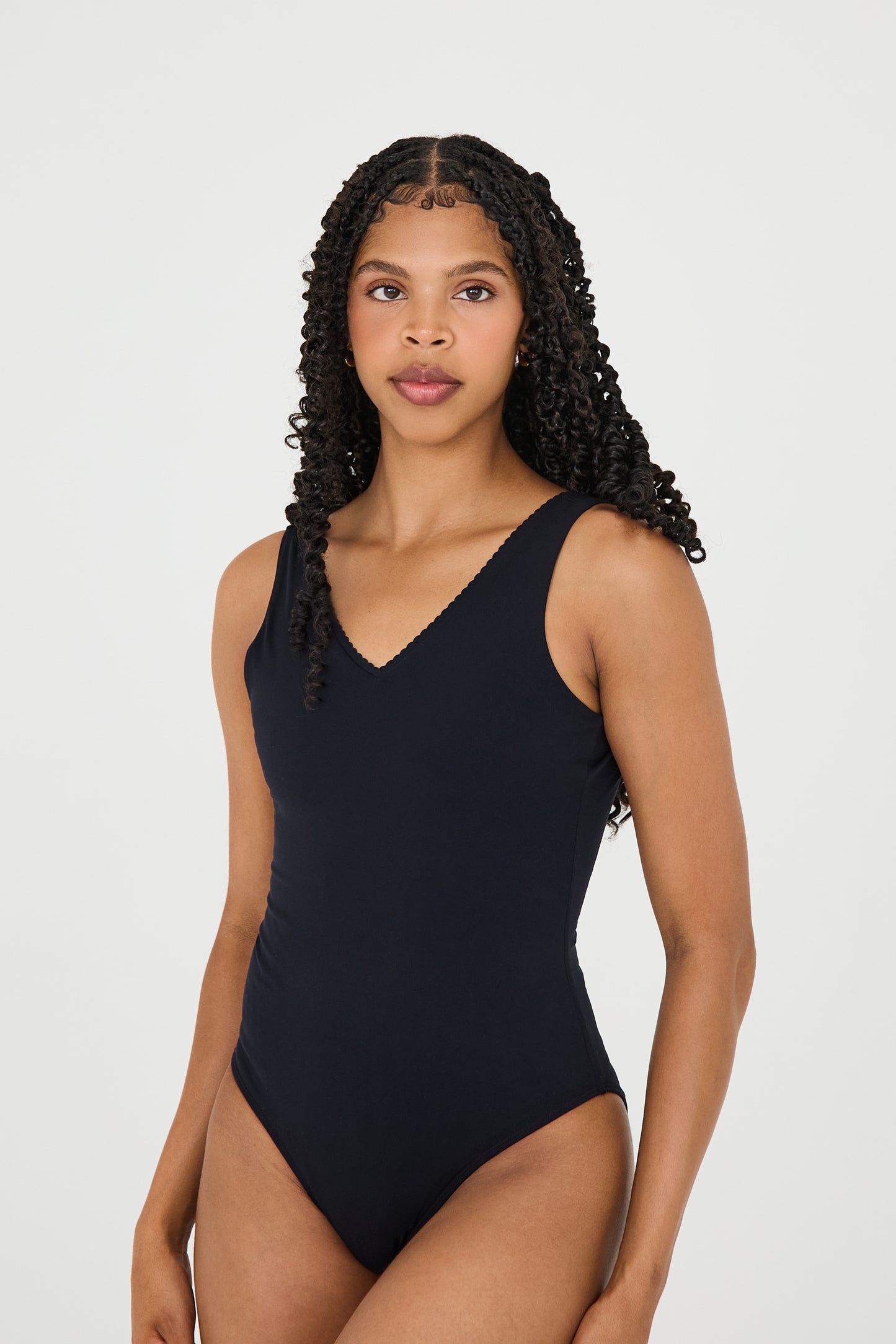 Model wearing the black Adorn Bodysuit from Elastique’s sculptural Adorn Collection, featuring a flattering décolleté neckline with scalloped trim, open back design, smooth, form-fitting silhouette designed for both swim and everyday wear. Made with UPF 50 fabric and infused with patented MicroPerle® beads for gentle lymphatic stimulation and core support