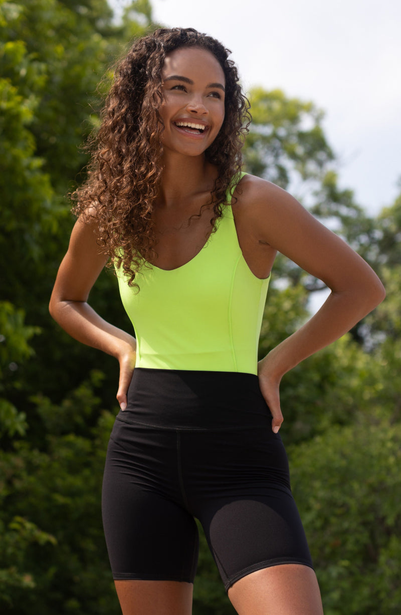Model wearing the Riviera Bodysuit in lime color, a sleek two-in-one swimsuit and bodysuit crafted from OEKO-TEX® certified compression fabric with patented MicroPerle® technology. Designed to smooth, sculpt, and support the body, it promotes lymphatic drainage and circulation while offering effortless elegance from poolside to dinner. A statement of clean luxury and wellness-infused style.