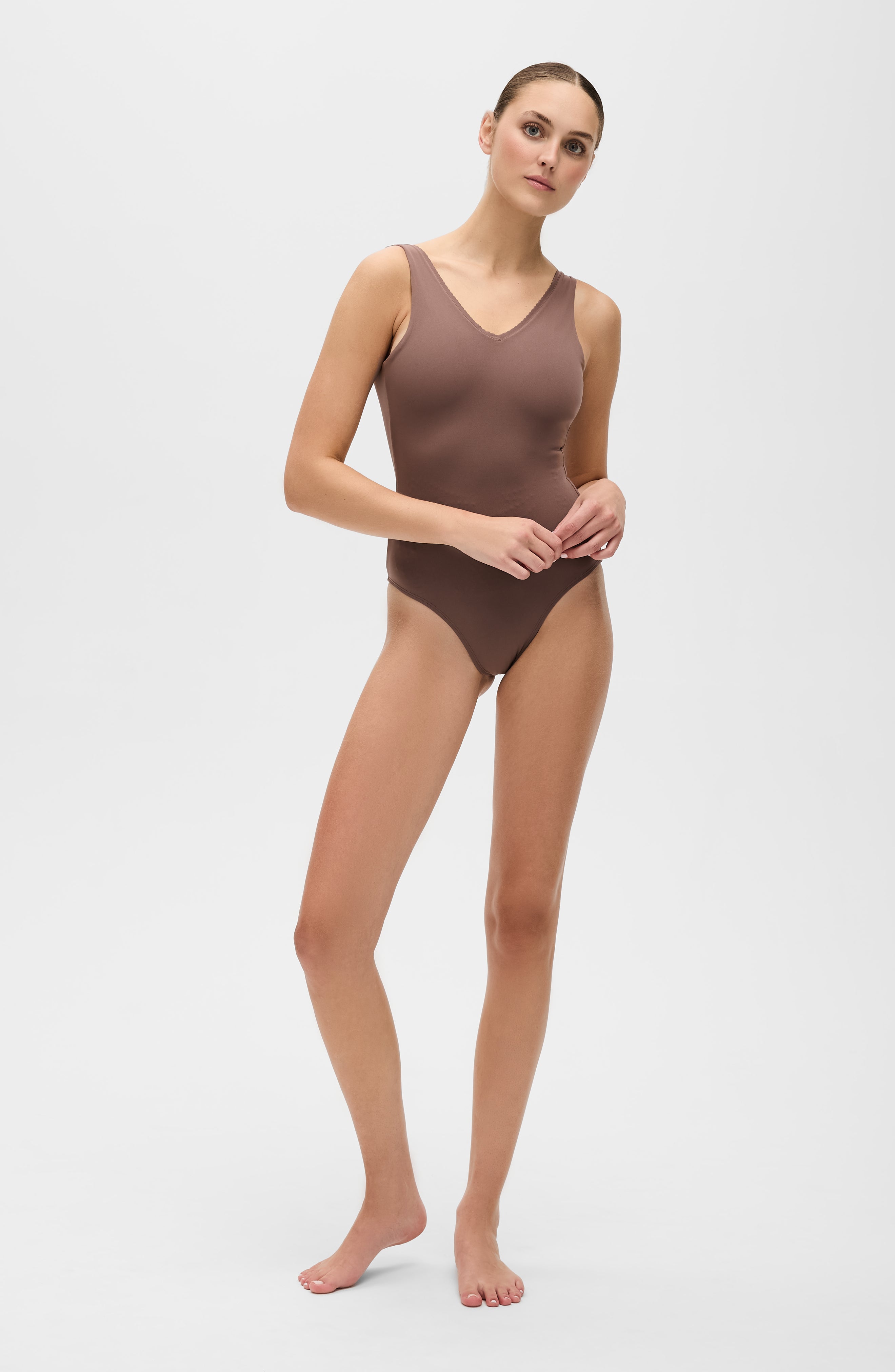 Model wearing the black Adorn Bodysuit from Elastique’s sculptural Adorn Collection, featuring a flattering décolleté neckline with scalloped trim, open-back design, and a smooth, form-fitting silhouette. Crafted with UPF 50 OEKO-TEX® fabric infused with patented MicroPerle® beads for gentle lymphatic stimulation, improved circulation, and core support.