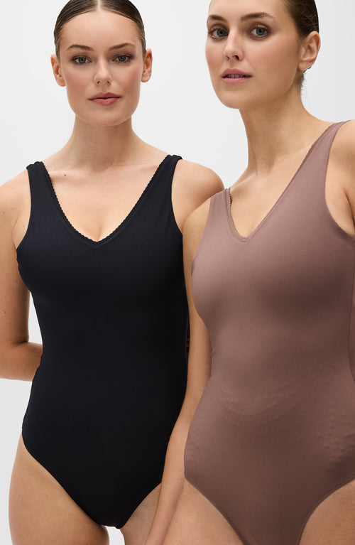 Load image 1 in gallery view. Models wearing the Adorn Bodysuit from Elastique’s sculptural Adorn Collection, featuring a flattering décolleté neckline with scalloped trim, open-back design, and a smooth, form-fitting silhouette. Crafted with UPF 50 OEKO-TEX® fabric infused with patented MicroPerle® beads for gentle lymphatic stimulation, improved circulation, and core support.
