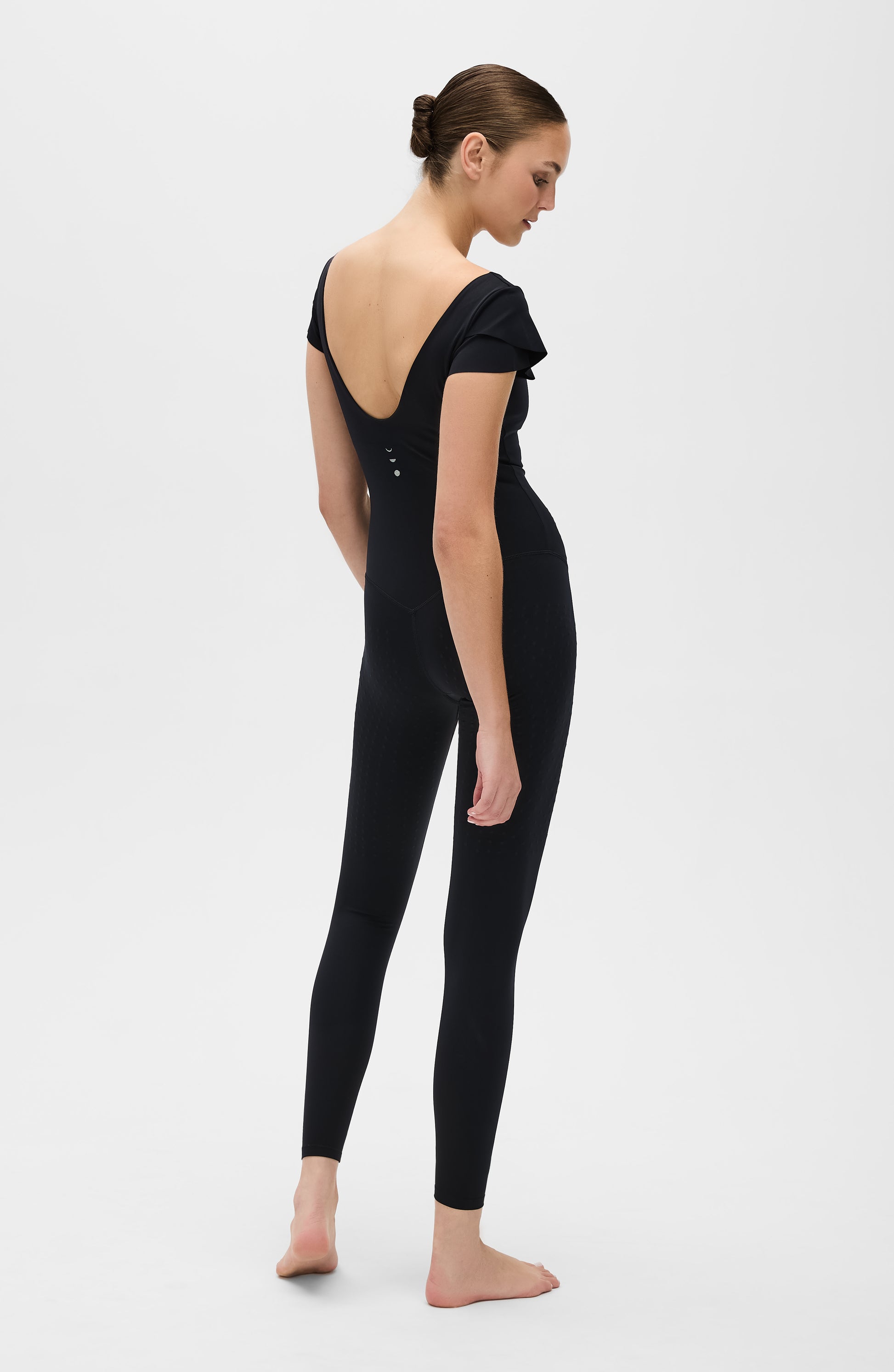 Le Cha-Cha jumpsuit in black featuring a sophisticated open back, delicate sleeve detailing, and a sleek, sculpting silhouette. Crafted from OEKO-TEX® certified compression fabric with Elastique’s MicroPerle® technology to promote lymphatic drainage, boost circulation, reduce fatigue, and enhance vitality.