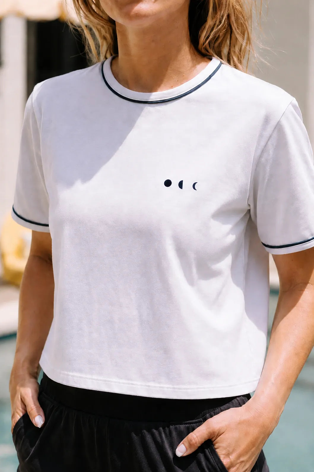 Close-up of a white cropped tee from the Monte Carlo collection featuring elegant navy trim and refined resort-inspired activewear styling for elevated everyday and poolside comfort.