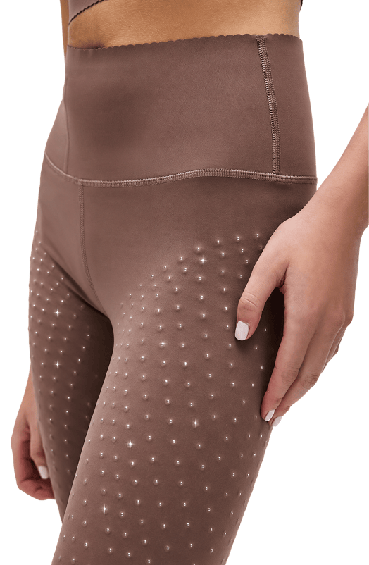 Close-up of a person wearing high-waisted brown leggings with micro pearl beads on the upper thighs, shown against a plain white background.
