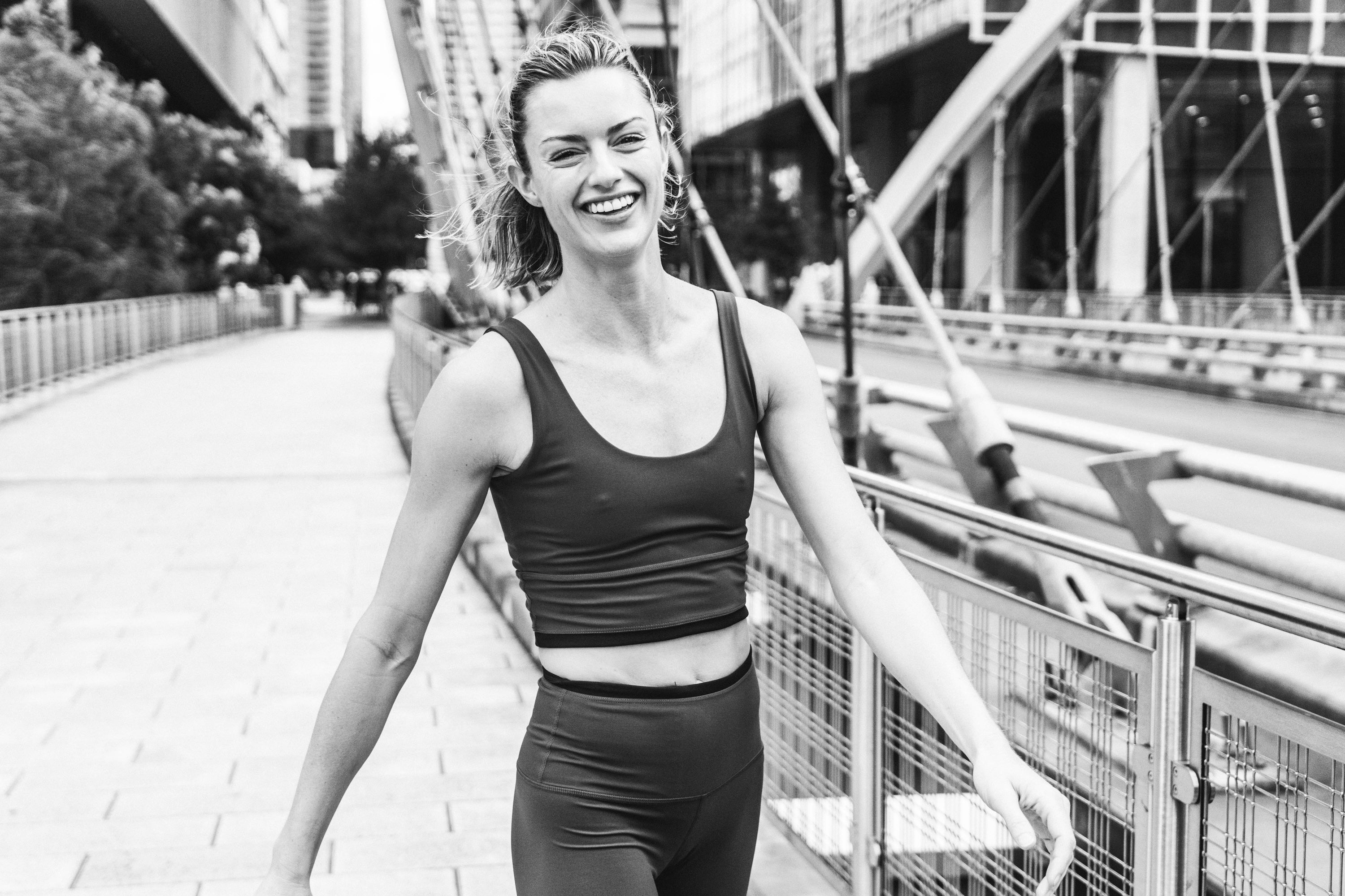 Black and white image of model smiling post run on city bridge.