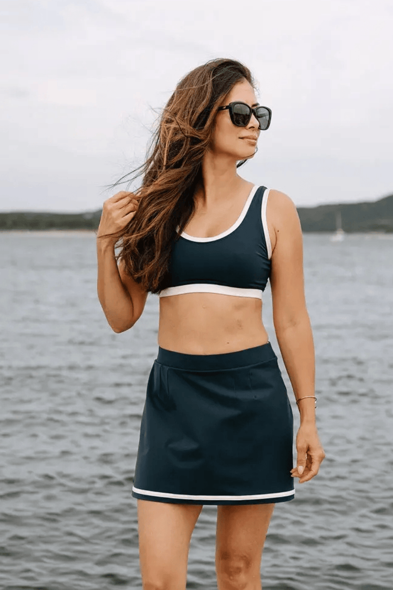Woman wearing a navy compression skort featuring MicroPerle® technology, designed to support lymphatic drainage and provide gentle shaping compression for comfort and recovery by the water.